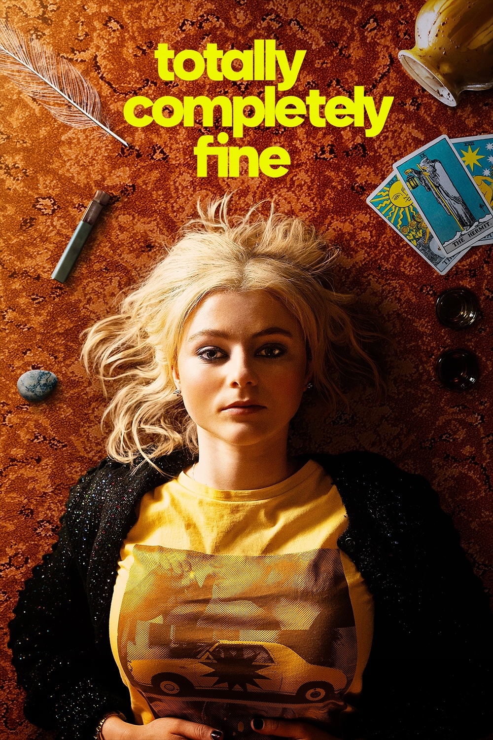 A blonde woman laying on the carpeted floor,looking up at the camera. Around her scatered tarot cards, drinking glasses, a feather and an urn