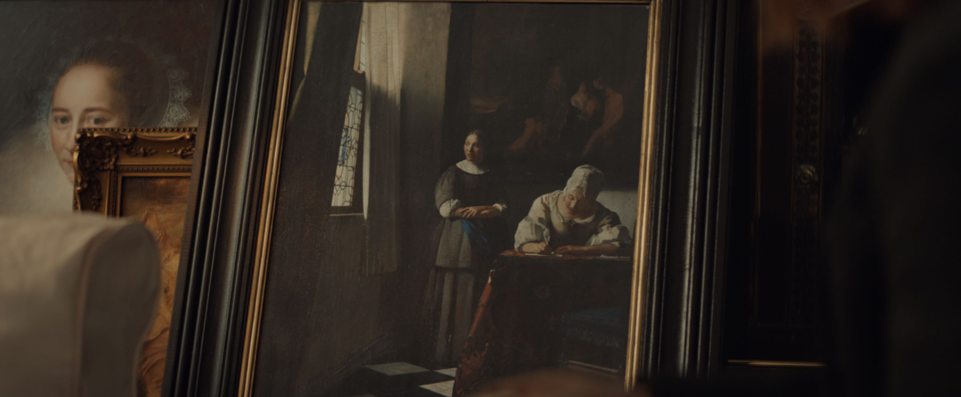 A stack of old paintings leaning against a wall. On top 'Lady Writing a Letter With Her Maid' by Vermeer.