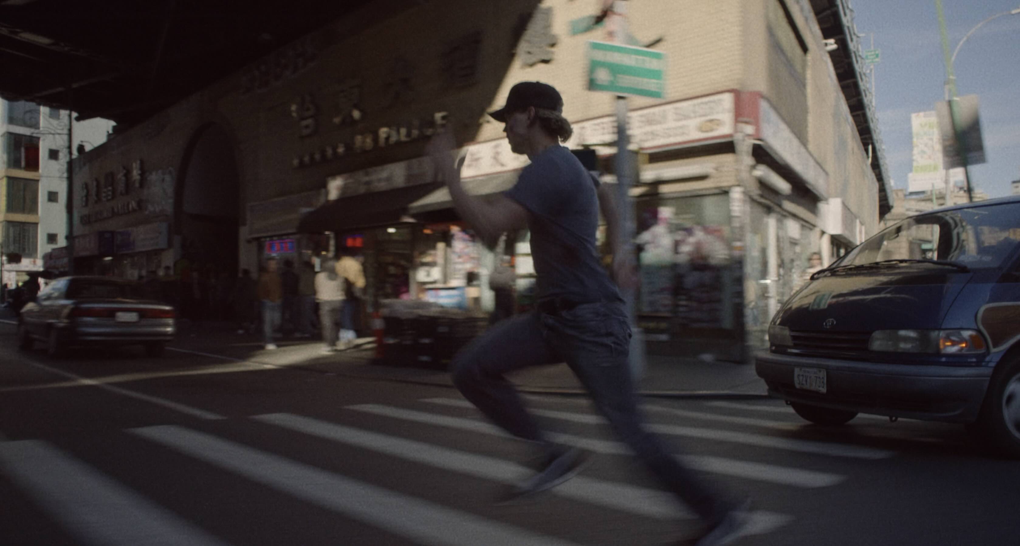 A man in a grey t-shirt and a black baseball cap runs frantically down an American city street.