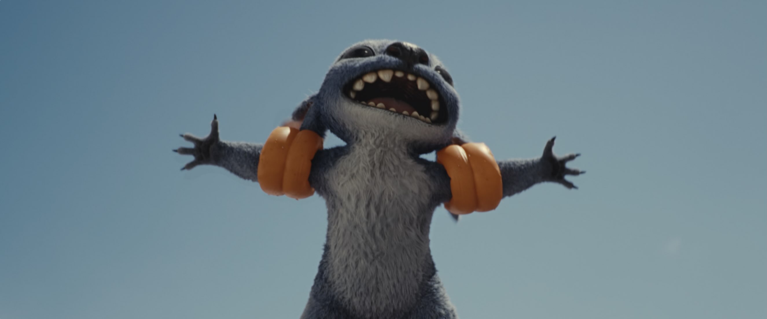 A small, blue, furry alien holds it's arms out wide with a big toothy grin on it's face. It's wearing orange water wings.