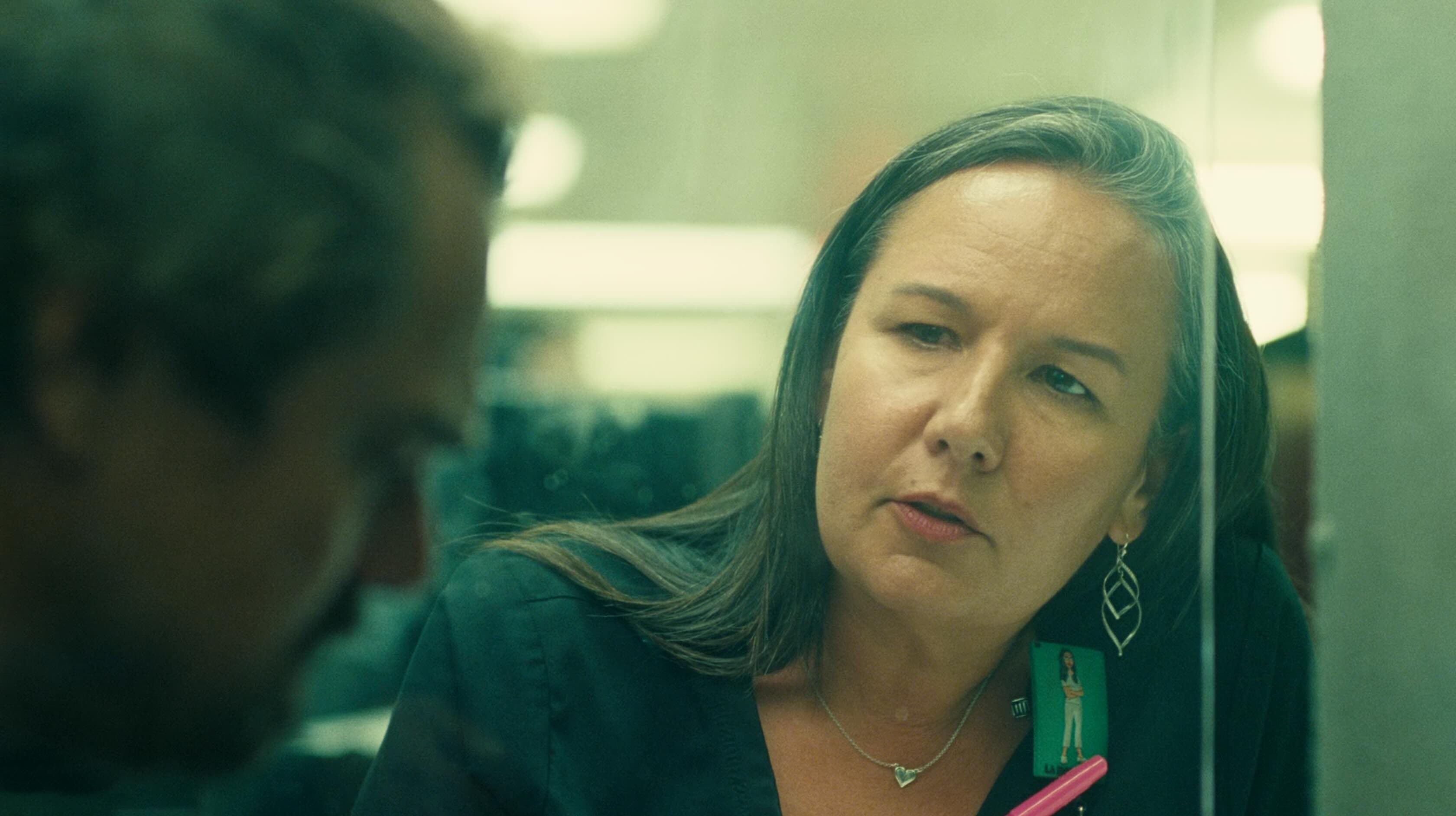 A middle aged, female nurse with an elegant grey streak in her hair looks at Leonardo DiCaprio through a clear perspex dividing screen.