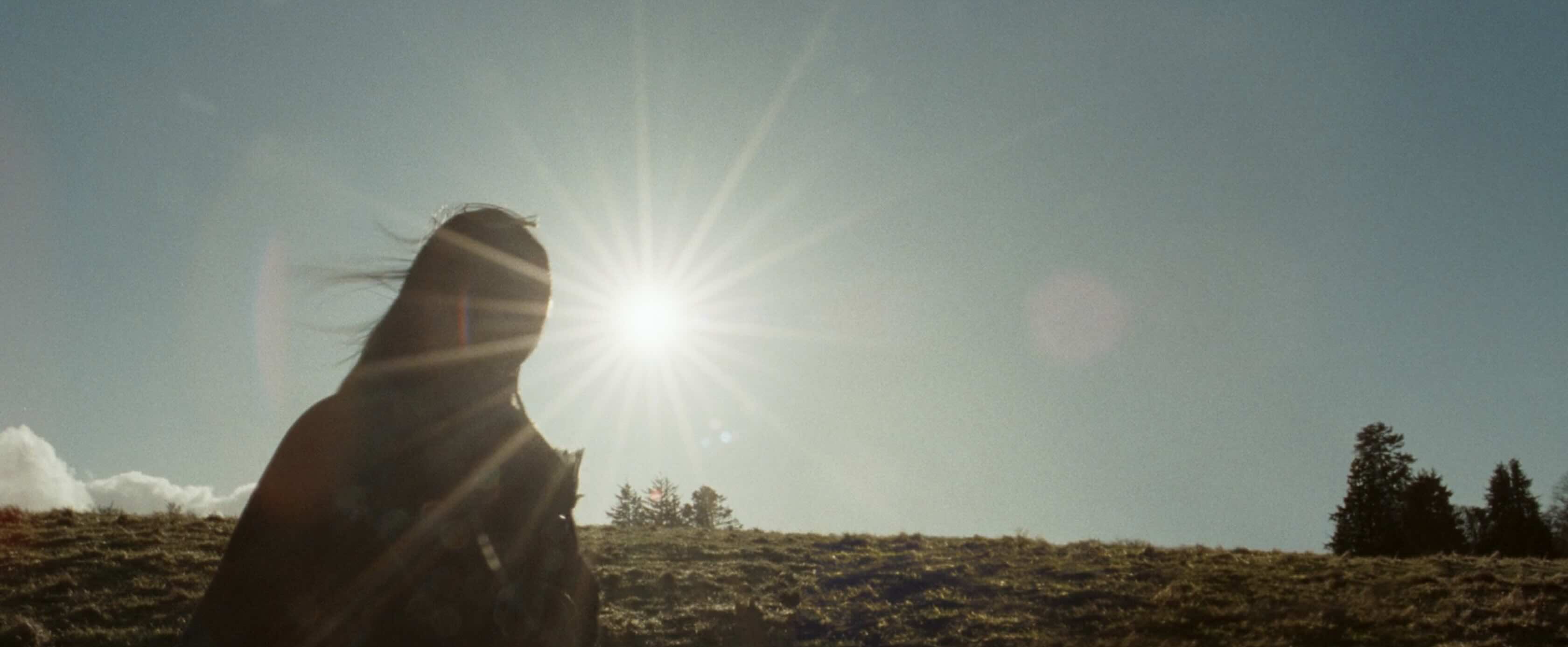 The bright sun on a clear, cold day, we can see a woman in silhouette in a green field