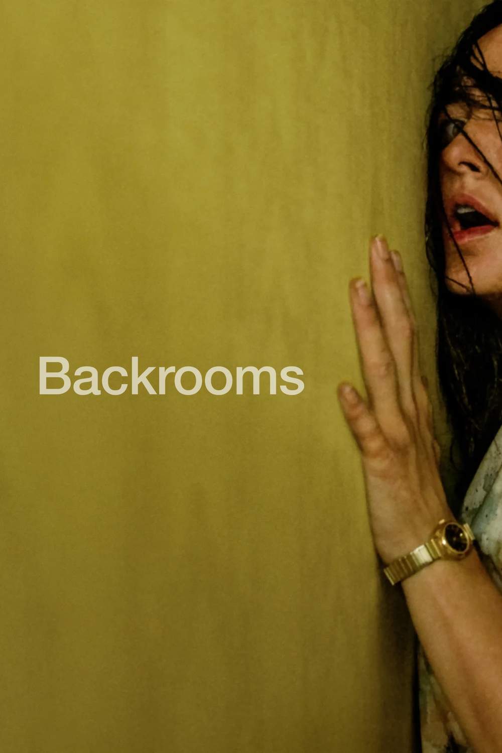 Poster for the film Backrooms. A young white woman wit brown hair is stood flat against a yellow wall, mouth agape. She's barely in the frame, with the wall taking up most of the image, giving the impression she is being squeezed into a tiny gap.