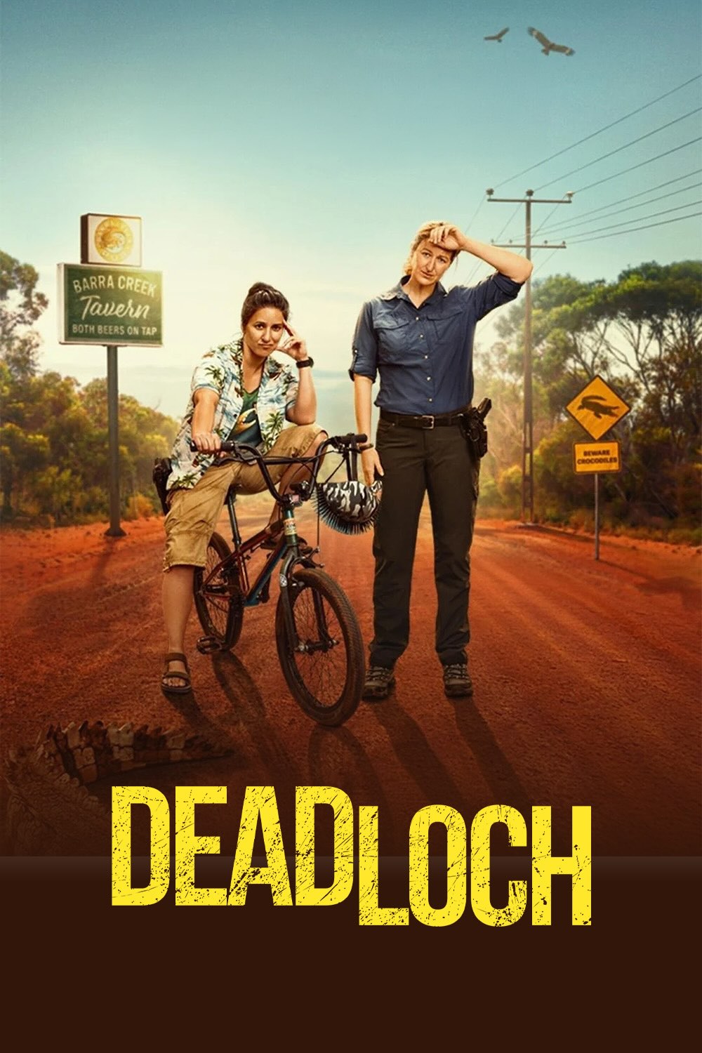Poster for the second series of Deadloch. A red dirt road in the sun drenched Australian outback. On it is a brunette wearing a Hawaiian shirt and sat on a BMX. to the right of her is a tall blond wearing a blue, long sleeve shirt, dark trousers and sensible boots. Unsurprisingly she's wiping sweat off her brow. There's a sign for the Barra Creek Tavern and another sign warning about crocodiles