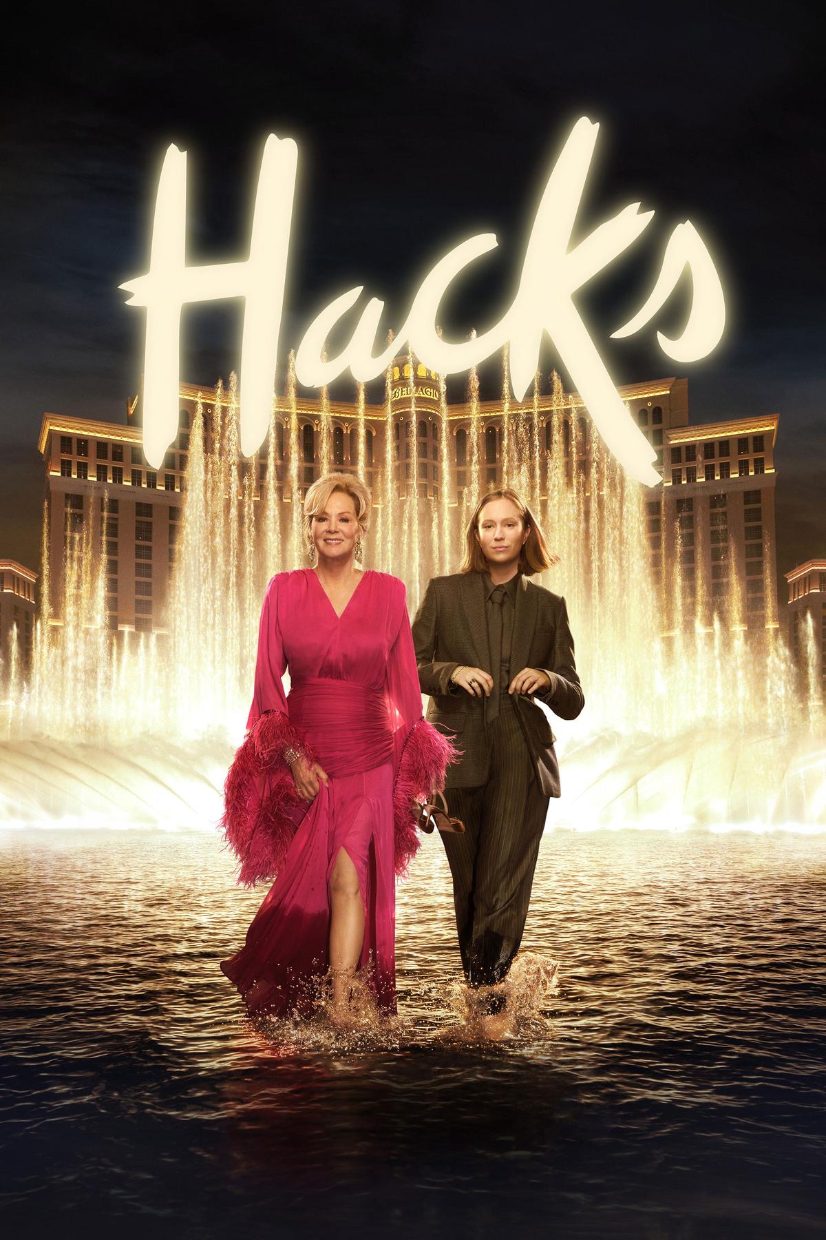 Poster for the tv show Hacks. A glamourous blonde, older woman walks next to a brunette in her late twenties, wearing a brown, tailored suit. They are walking through the water of a fountain, kicking up water and looking pleased with themselves. The lights of night time Las Vegas are in the background.