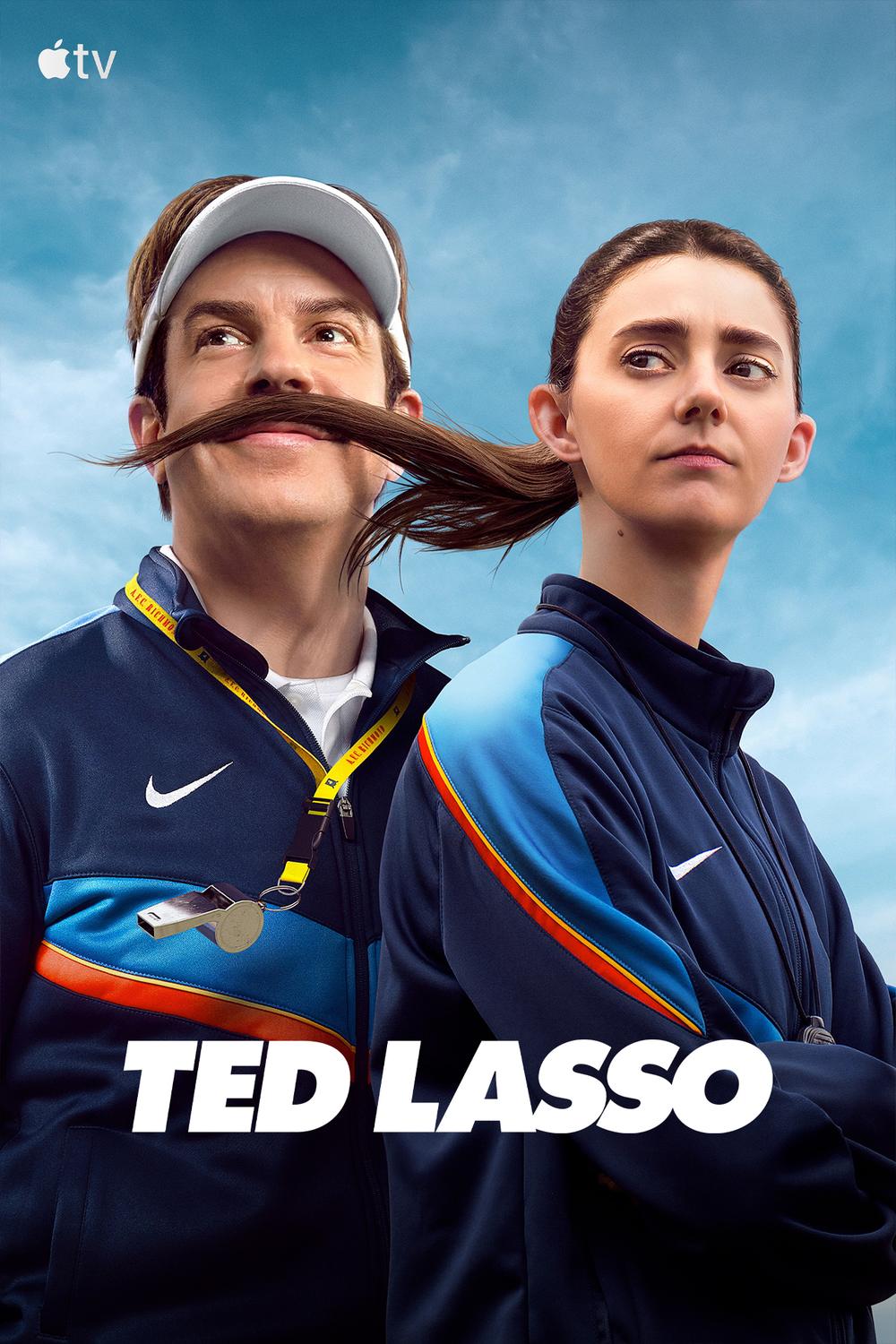 Poster for the tv show Ted Lasso. Head and shoulders shot of a middle aged man and a younger woman, against a blue sky background. Both are wearing blue tracksuits. He's wearing a white sun visor, her pony tail is blowing across his face and it looks like an elaborate moustache.
