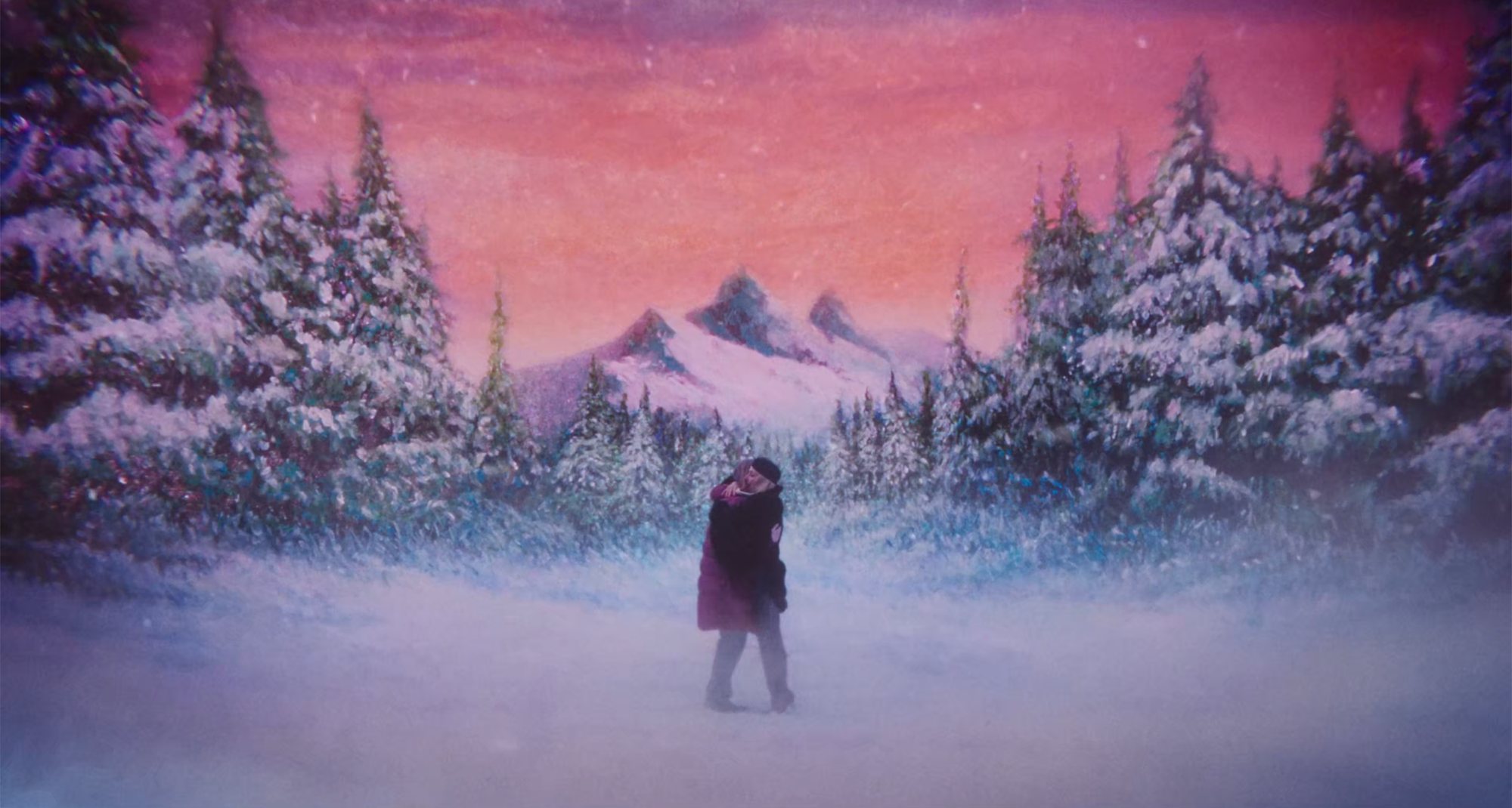 The same pink tinged snow scene but from a wider angle, the two women hug each other tightly. The background looks like a painting, the sunset over the mountains is pink and red and orange.