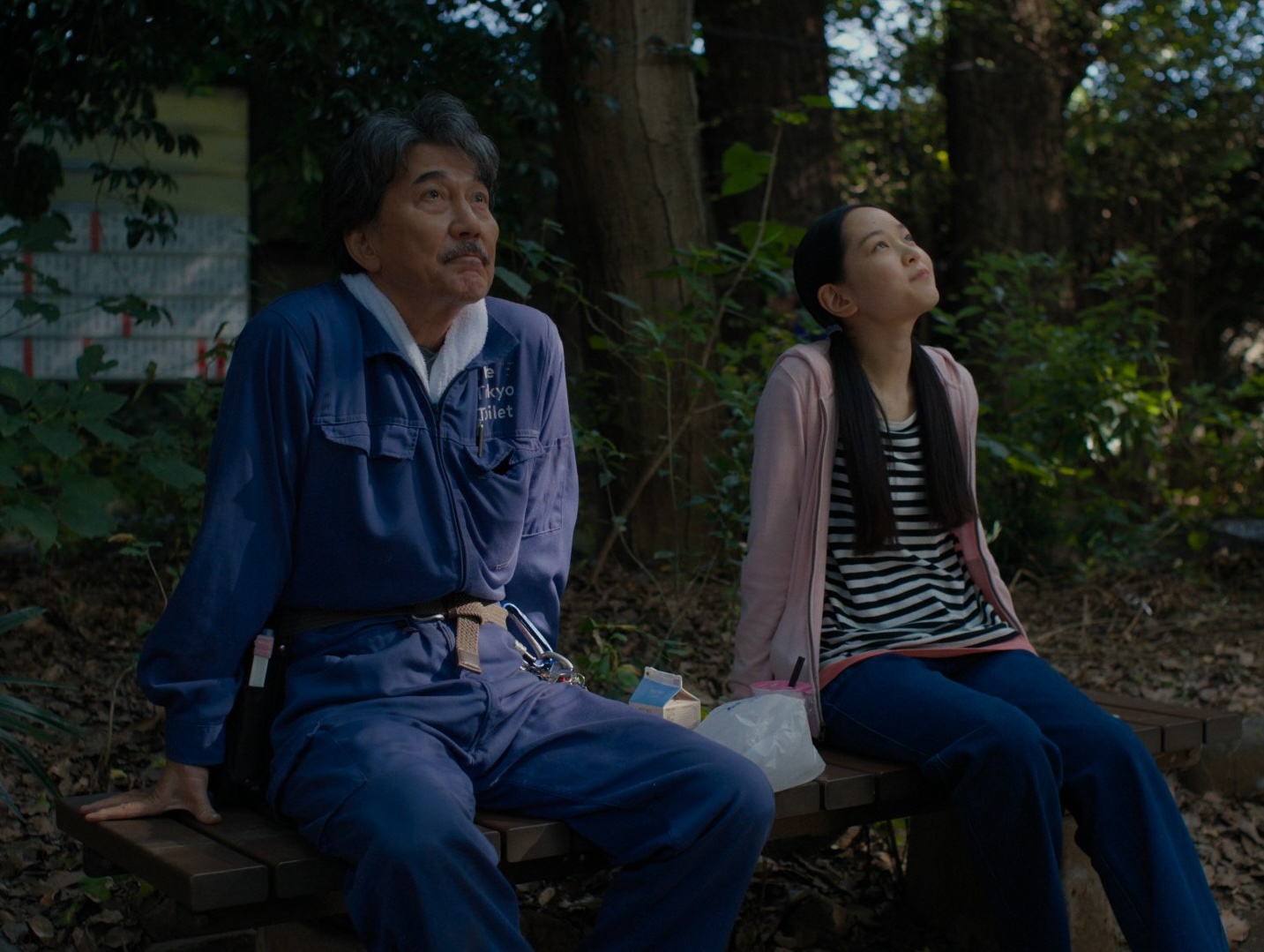 The same scene as the poster, but this time there's a dark haired, preteen girl sat next to him, also looking upwards.