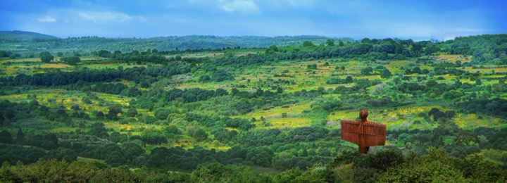 a wide shot of the English countryside featuring the Angel of the North, a industrial steel statue, watching over it